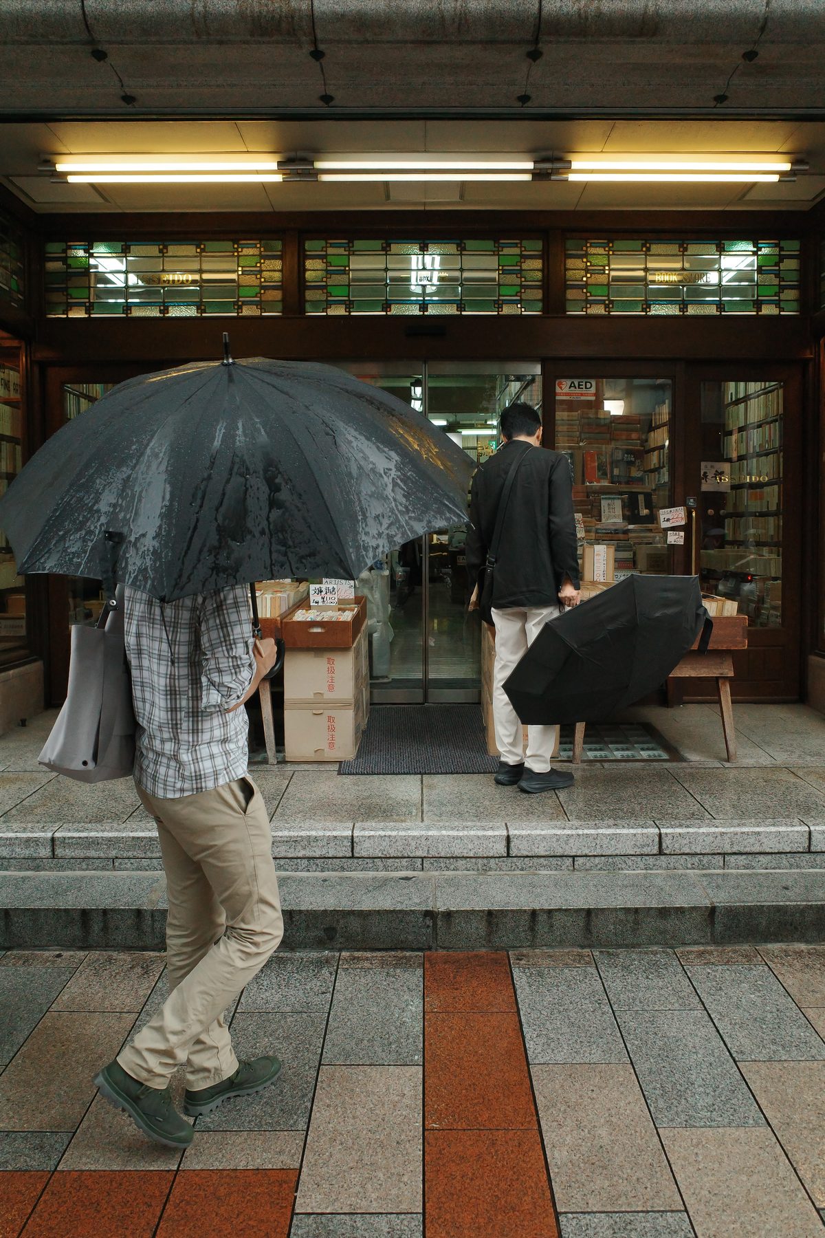 A man under a black umbrella at a bookshop