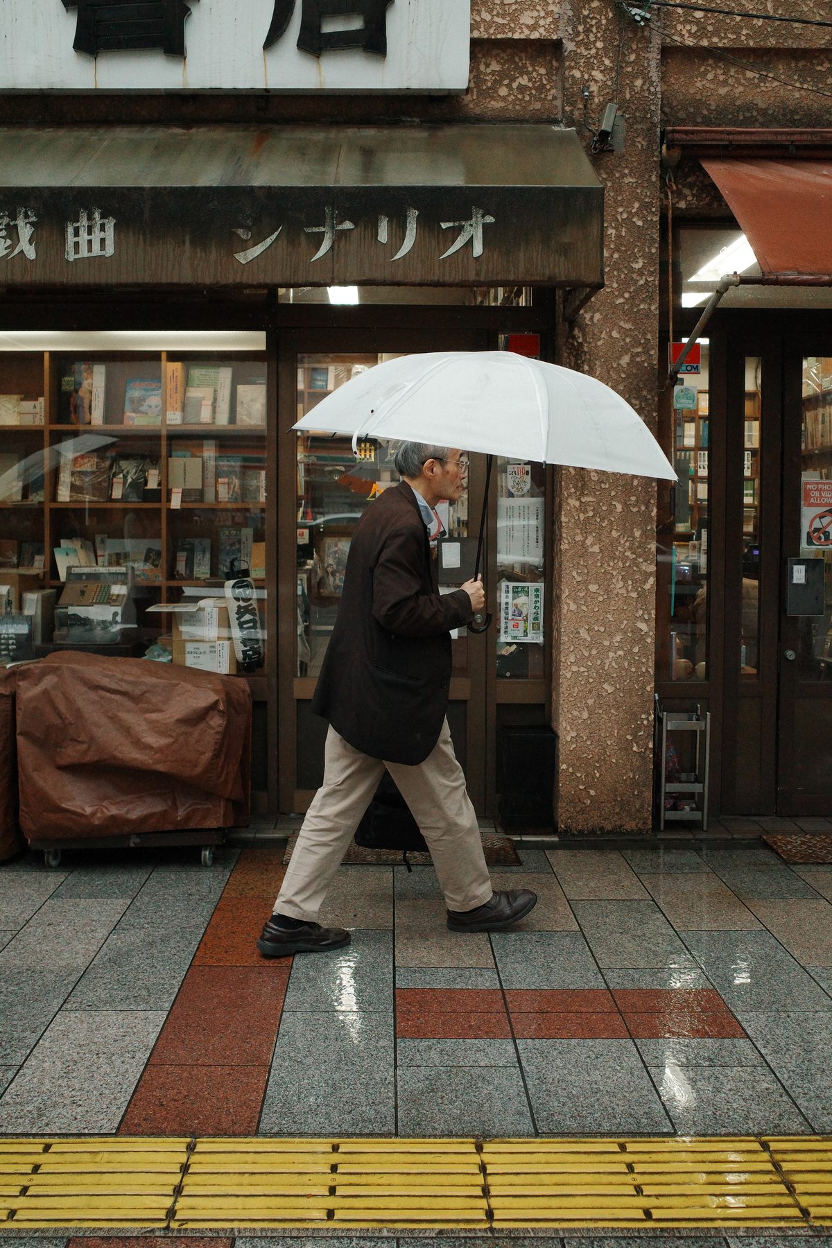 A man with a white umbrella passing a bookshop