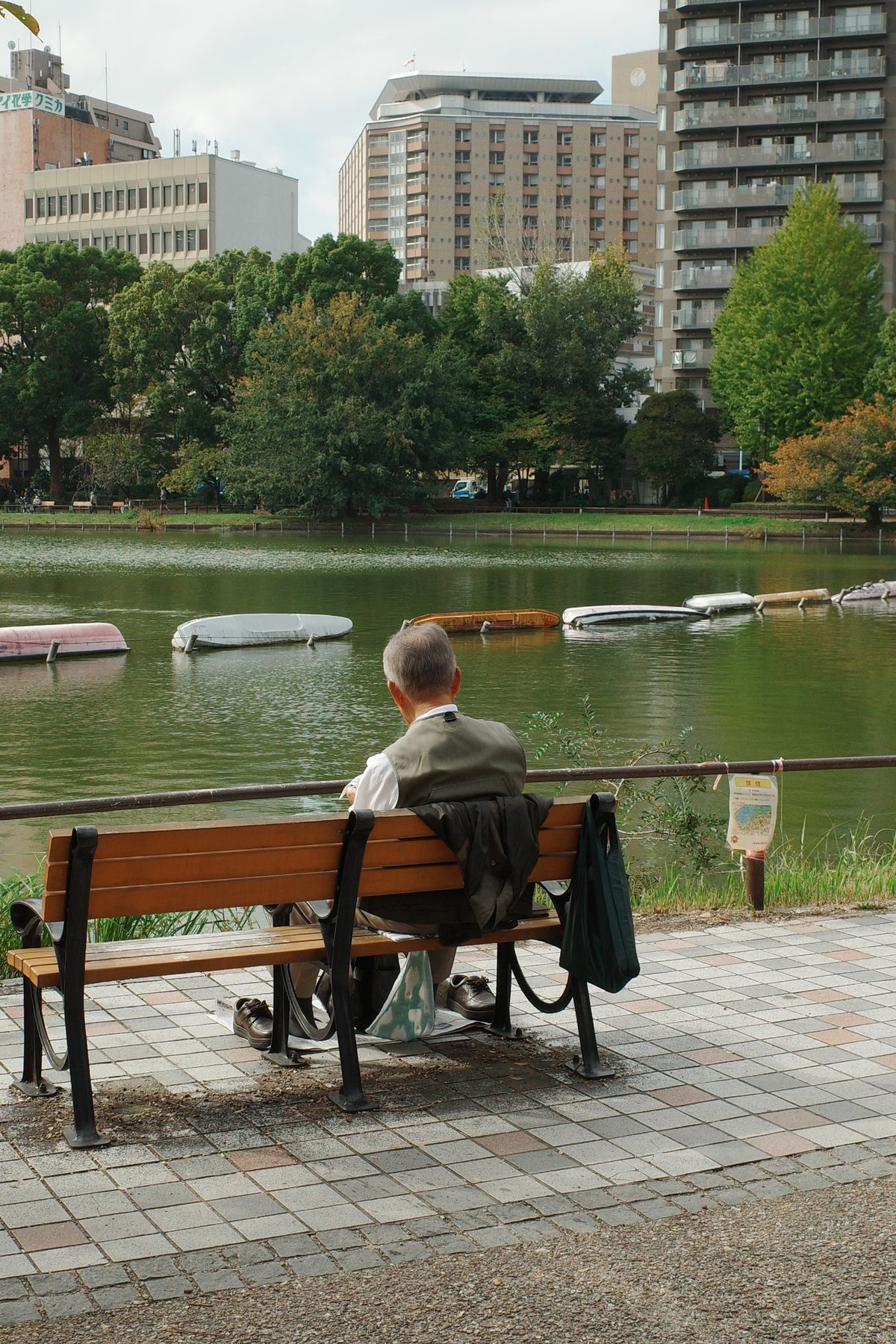 A man on a bench by a pond, towers behind
